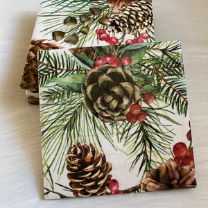 May include: Set of four square coasters with a white background and a wintery pine cone and berry design. The coasters feature brown pine cones, green pine needles, and red berries.