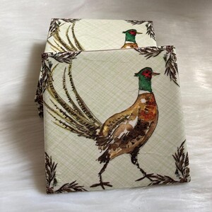 May include: Set of four coasters featuring a pheasant with a green head and brown and white feathers on a cream background with a brown and white plaid pattern. The coasters have a brown border with a leafy design.