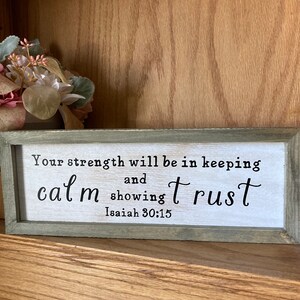May include: A wooden sign with a white background and black text. The text reads "Your strength will be in keeping calm and showing trust. Isaiah 30:15".