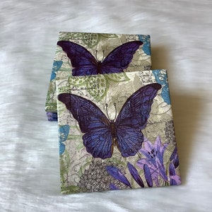 May include: Set of four coasters featuring a purple butterfly design on a white background with green and blue accents. The coasters have a vintage, floral pattern.