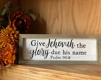 May include: A wooden sign with a white background and black lettering. The sign reads "Give Jehovah the glory due his name Psalm 96:8".
