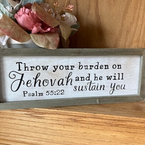 May include: A wooden sign with a white background and black text. The sign reads "Throw your burden on Jehovah and he will sustain you. Psalm 55:22".