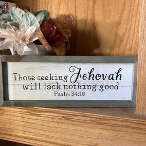 May include: A wooden sign with a white background and black lettering. The sign reads "Those seeking Jehovah will lack nothing good" and "Psalm 34:10". The sign is framed in a gray wood frame.