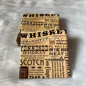 May include: A stack of four brown and beige coasters with a vintage newspaper design. The coasters feature text about different types of whiskey, including Tennessee whiskey, Scotch whiskey, and bourbon. The text includes the words "straight up", "on the rocks", and "neat".