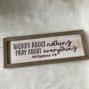May include: Wooden sign with the text "Worry about nothing, pray about everything, Philippians 4:6" in black lettering.
