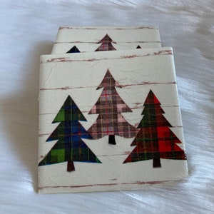 May include: Set of four coasters featuring a white background with a wood grain pattern. Each coaster has a different plaid Christmas tree design in red, green, and blue.