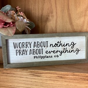 May include: A wooden sign with the text "Worry about nothing, pray about everything, Philippians 4:6" in black lettering on a white background.