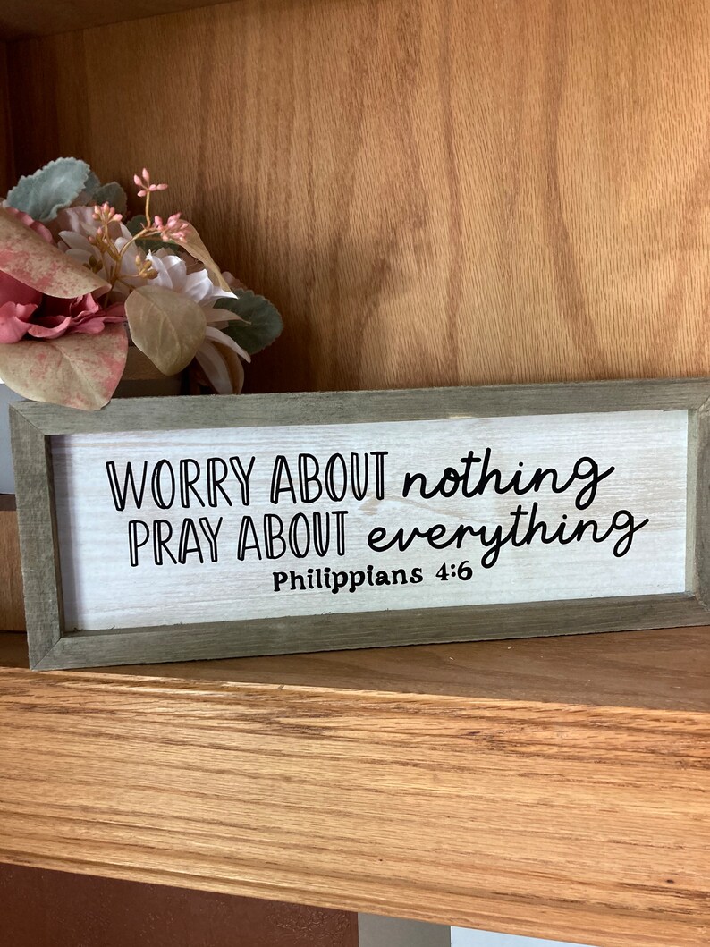 May include: A wooden sign with the text "Worry about nothing, pray about everything, Philippians 4:6" in black lettering on a white background.
