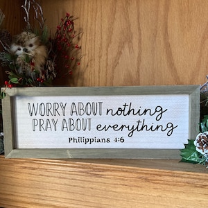May include: A wooden sign with the text "Worry about nothing Pray about everything Philippians 4:6" in black lettering on a white background.