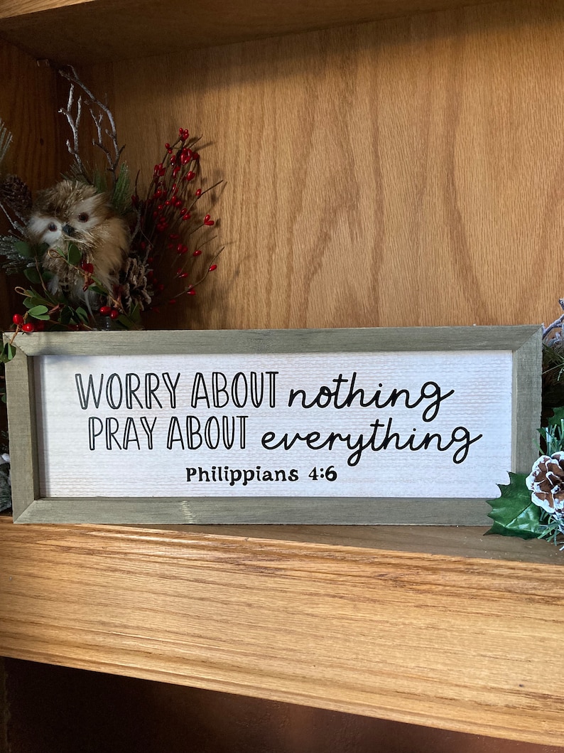 May include: A wooden sign with the text "Worry about nothing Pray about everything Philippians 4:6" in black lettering on a white background.