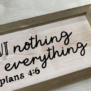 May include: A wooden sign with white paint and black lettering that reads "But nothing is everything" with the scripture Philippians 4:6 below.