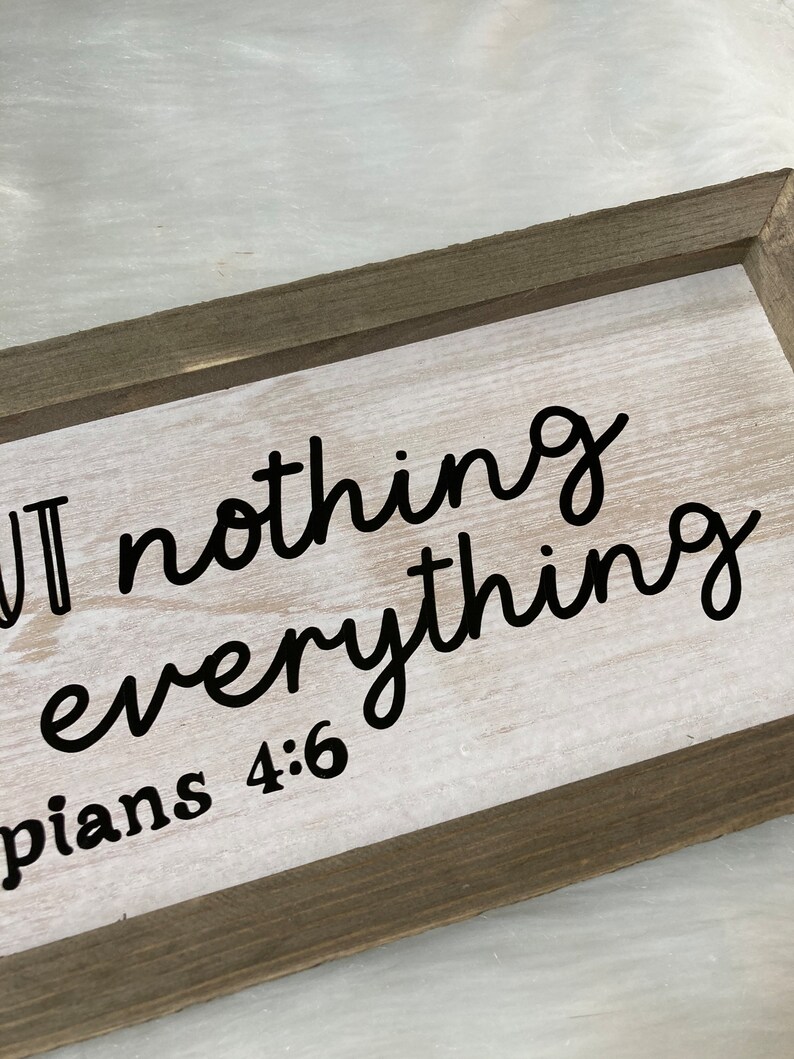 May include: A wooden sign with white paint and black lettering that reads "But nothing is everything" with the scripture Philippians 4:6 below.