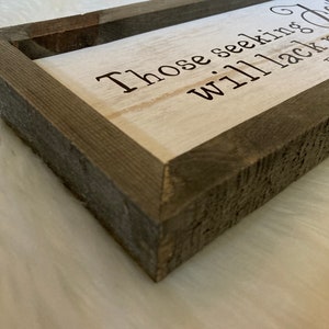 May include: A rustic wooden sign with a white background and brown wood frame. The sign reads "Those seeking... will lack nothing".