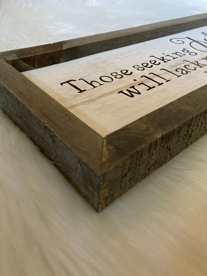 May include: A rustic wooden sign with a white background and brown wood frame. The sign reads "Those seeking... will lack nothing".