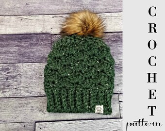 May include: A green crochet beanie with a brown faux fur pom pom. The beanie has a textured stitch pattern and a small tag with the word "Shop" on it. CROCHET pattern.