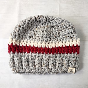 May include: Gray crocheted beanie with a red, white, and cream stripe. The beanie has a small brown tag with the text "Cozy Dreams" on it.