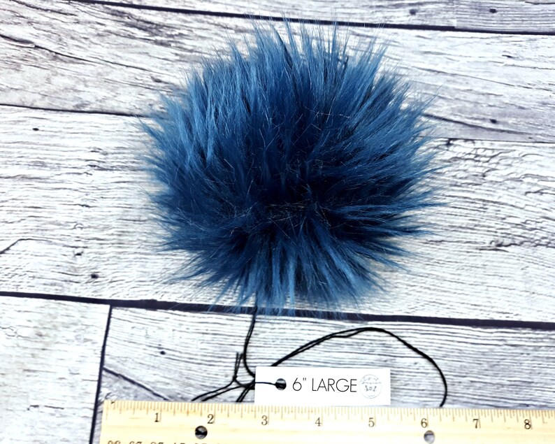 Puede incluir: Un gran pomp&oacute;n de piel sint&eacute;tica azul marino y esponjoso. El pomp&oacute;n mide aproximadamente 15 cm de di&aacute;metro. Una etiqueta adjunta al pomp&oacute;n dice "6" LARGE". El pomp&oacute;n est&aacute; sobre una superficie de madera blanca y azul claro.