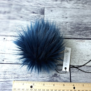 Puede incluir: Un pomp&oacute;n de piel sint&eacute;tica azul marino, de aproximadamente 13 cm de di&aacute;metro, con una etiqueta que dice "5" MEDIUM". El pomp&oacute;n es redondo y esponjoso, con fibras largas y puntiagudas. El fondo es una superficie de madera clara.
