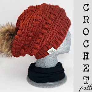 Op de afbeelding: Een gebreide beanie muts in een roestoranje kleur met een nep bont pompon. De muts zit op een grijs mannequin hoofd met een zwarte sjaal om de nek. De tekst "CROCHET pattern" staat aan de rechterkant van de afbeelding.