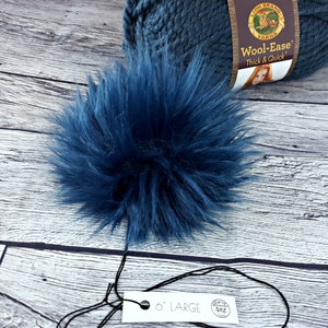 Puede incluir: Un pomp&oacute;n grande y esponjoso de color azul marino con una etiqueta que dice "6" LARGE". Una madeja de lana Wool-Ease Lion Brand azul marino est&aacute; en el fondo. El pomp&oacute;n est&aacute; hecho de suave piel sint&eacute;tica y es un suministro artesanal.