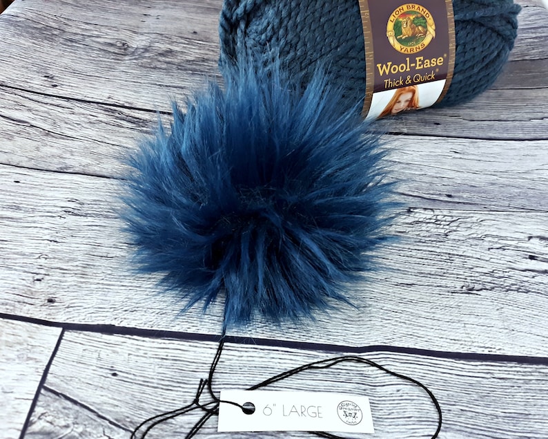 Puede incluir: Un pomp&oacute;n grande y esponjoso de color azul marino con una etiqueta que dice "6" LARGE". Una madeja de lana Wool-Ease Lion Brand azul marino est&aacute; en el fondo. El pomp&oacute;n est&aacute; hecho de suave piel sint&eacute;tica y es un suministro artesanal.