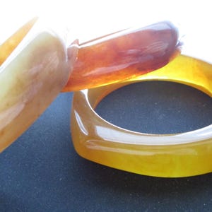 K&ouml;nnte beinhalten: Drei armb&auml;nder in bernsteinfarben. Die Armb&auml;nder haben eine glatte, gl&auml;nzende Oberfl&auml;che und variieren in den Farbt&ouml;nen von hellgelb bis tiefbraun. Die Armb&auml;nder bestehen aus einem durchscheinenden Material, durch das Licht hindurchscheinen kann. Die Armb&auml;nder sind ein Modeaccessoire.