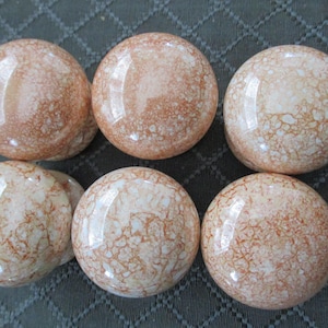 May include: Six round cabinet knobs with a glossy finish, featuring a marbled pattern of white and light orange veins. The knobs are arranged in two rows of three, with a silver-colored coin placed next to the bottom right knob for scale.