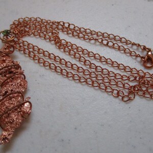 May include: A copper-colored necklace featuring a pendant with a textured, spiral design wrapped in copper wire. The necklace has a matching chain with a lobster clasp. The pendant is approximately 2 inches long.