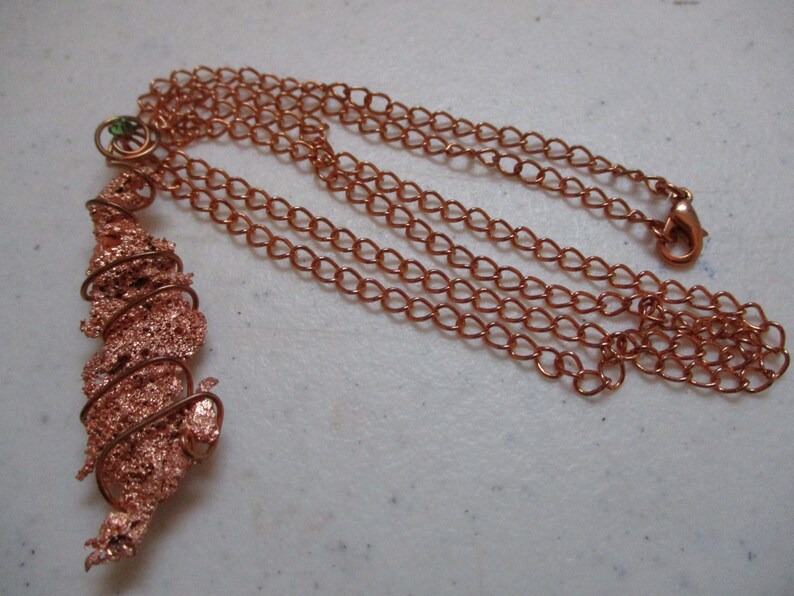 May include: A copper-colored necklace featuring a pendant with a textured, spiral design wrapped in copper wire. The necklace has a matching chain with a lobster clasp. The pendant is approximately 2 inches long.