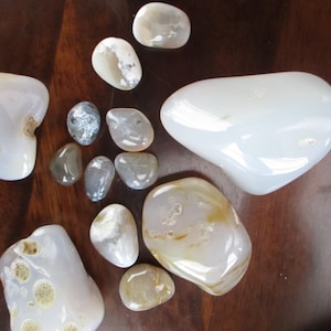 May include: A collection of twelve polished, smooth, tumbled stones in various sizes and shapes. The stones are primarily translucent white, milky, and light gray, with some featuring subtle tan, brown, or dark gray inclusions and patterns.