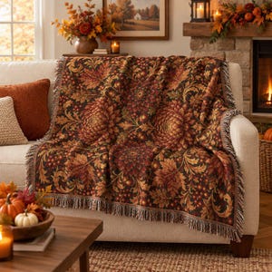 May include: A woven throw blanket featuring a dark brown background with a repeating pattern of large, detailed orange, red, and gold chrysanthemum flowers and swirling foliage. The blanket has a textured finish and a fringed edge along the sides.
