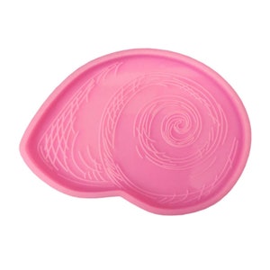 May include: A pink, seashell-shaped mold with a spiral design. The mold is made of a flexible material and is designed for crafting. The seashell shape is detailed with etched lines, creating a textured appearance. The overall design is simple and elegant.