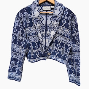 May include: A blue and white cropped jacket with a geometric pattern. The jacket has a single button closure and a collar. The label on the jacket reads "Flashback."
