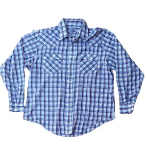 Puede incluir: Una camisa de manga larga a cuadros azules y blancos con un acento rojo. La camisa tiene dos bolsillos en el pecho con cierre de botón y un cuello puntiagudo.