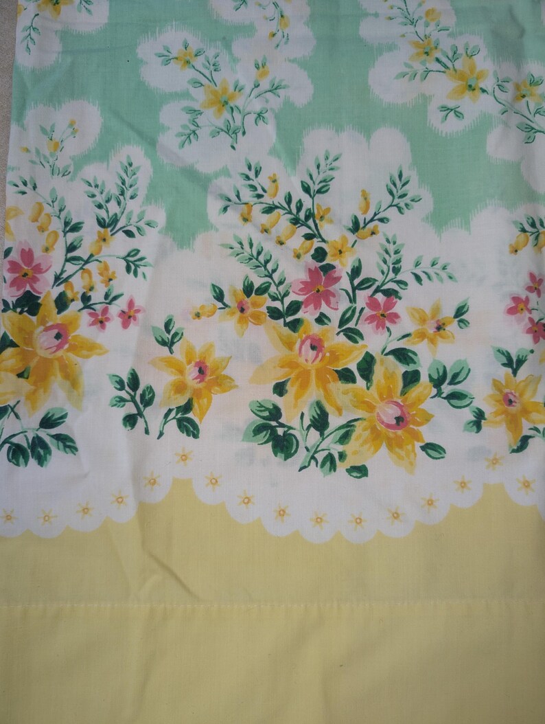 Pode incluir: Tecido floral com um padr&atilde;o repetido de flores amarelas e rosas, folhas verdes e formas brancas em forma de nuvem sobre um fundo verde claro. A borda inferior &eacute; amarela com uma borda branca ondulada.