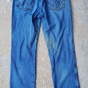 Puede incluir: Un par de pantalones vaqueros azules de mezclilla con una etiqueta Wrangler de cuero marr&oacute;n en el bolsillo trasero.