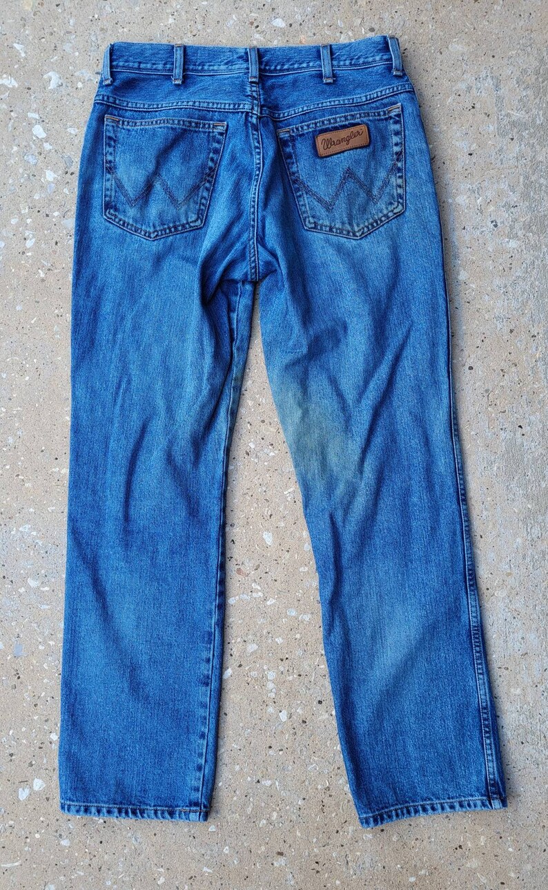 Puede incluir: Un par de pantalones vaqueros azules de mezclilla con una etiqueta Wrangler de cuero marr&oacute;n en el bolsillo trasero.