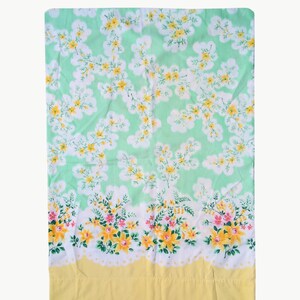 Pode incluir: Um len&ccedil;ol retangular com estampa floral. O fundo &eacute; verde claro, com flores brancas, amarelas e rosas. A borda inferior &eacute; amarela com uma borda ondulada branca.
