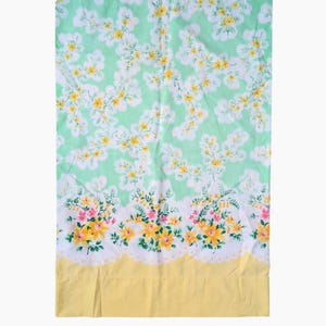 Pode incluir: Um len&ccedil;ol floral vintage. Possui um fundo verde claro com um padr&atilde;o de flores brancas e amarelas. A borda inferior apresenta uma borda amarela e uma guarni&ccedil;&atilde;o floral com flores rosa e amarelas.