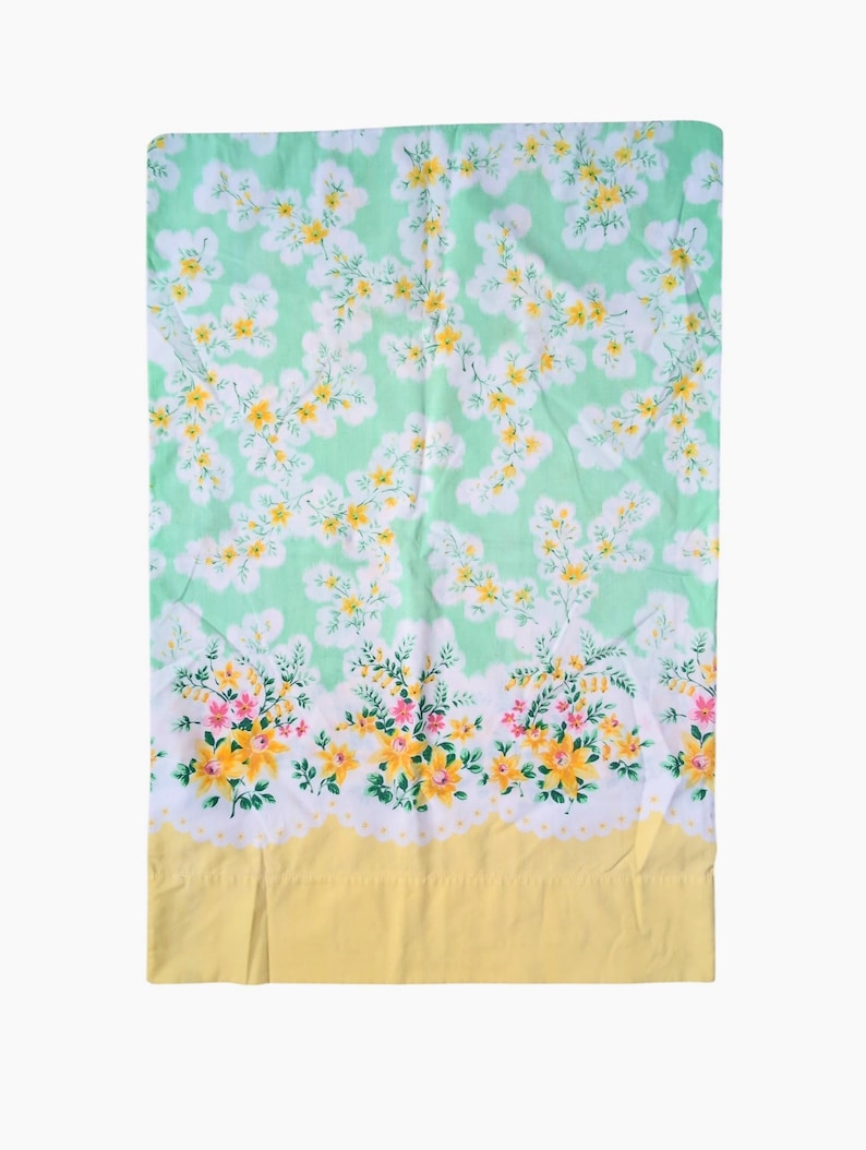 Pode incluir: Um len&ccedil;ol floral vintage. Possui um fundo verde claro com um padr&atilde;o de flores brancas e amarelas. A borda inferior apresenta uma borda amarela e uma guarni&ccedil;&atilde;o floral com flores rosa e amarelas.