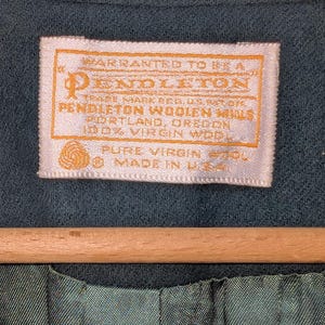 May include: Close-up of a teal-colored garment with a rectangular label. The label, in shades of cream and gold, reads "PENDLETON WOOLEN MILLS, PORTLAND, OREGON, 100% VIRGIN WOOL, MADE IN U.S.A."