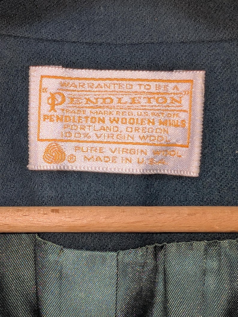May include: Close-up of a teal-colored garment with a rectangular label. The label, in shades of cream and gold, reads "PENDLETON WOOLEN MILLS, PORTLAND, OREGON, 100% VIRGIN WOOL, MADE IN U.S.A."