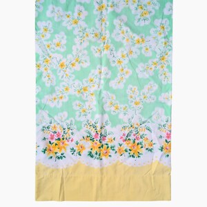 Pode incluir: Um len&ccedil;ol floral vintage com fundo verde claro e um padr&atilde;o de flores brancas e amarelas. A borda inferior apresenta uma borda amarela e uma guarni&ccedil;&atilde;o floral com flores rosa e amarelas.