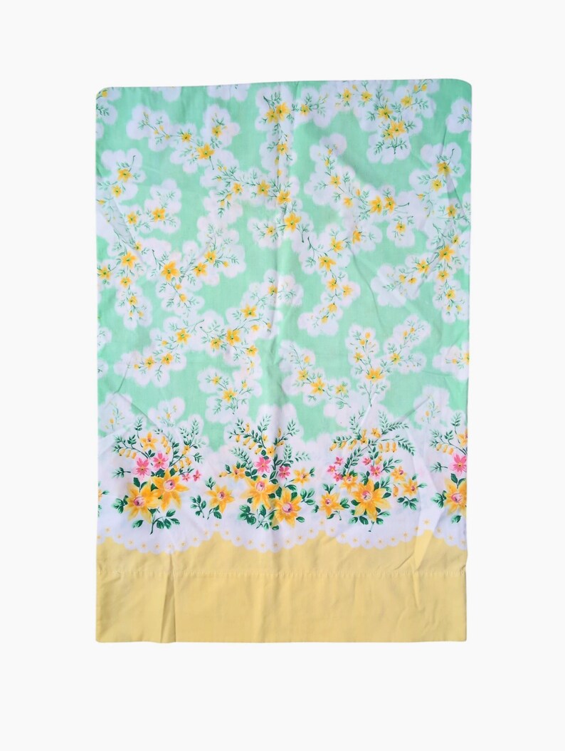 Pode incluir: Um len&ccedil;ol floral vintage com fundo verde claro e um padr&atilde;o de flores brancas e amarelas. A borda inferior apresenta uma borda amarela e uma guarni&ccedil;&atilde;o floral com flores rosa e amarelas.
