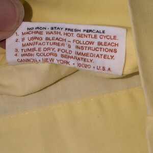 Pode incluir: Close-up de um tecido amarelo com uma etiqueta branca. A etiqueta tem o texto "NO IRON - STAY FRESH PERCALE" e instru&ccedil;&otilde;es de lavagem. A etiqueta tamb&eacute;m inclui a marca "CANNON, NEW YORK, 10020, U.S.A."