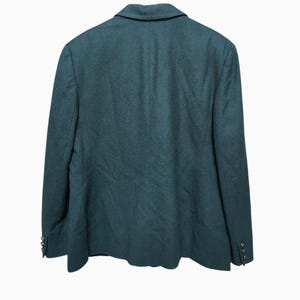 May include: A dark teal blazer with a classic notched lapel and two decorative buttons on each cuff. The back of the blazer is visible, showcasing the tailored design and fabric texture. The blazer is a solid color, suitable for various occasions.