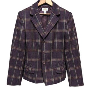 Pode incluir: Um blazer marrom com um padrão xadrez em tons de bege, verde e roxo. O blazer tem um colarinho de entalhe, fecho de dois botões e dois bolsos de aba.