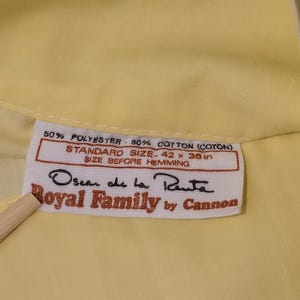 Pode incluir: Um close-up de um tecido amarelo com uma etiqueta. A etiqueta diz "50% POLYESTER 50% COTTON (COTON)", "STANDARD SIZE-106.68 x 91.44 cm" e "Oscar de la Renta Royal Family by Cannon".