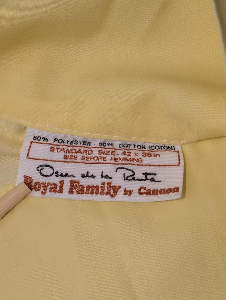 Pode incluir: Um close-up de um tecido amarelo com uma etiqueta. A etiqueta diz "50% POLYESTER 50% COTTON (COTON)", "STANDARD SIZE-106.68 x 91.44 cm" e "Oscar de la Renta Royal Family by Cannon".