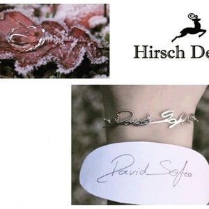 Puede incluir: Una pulsera de plata con el nombre "David Sofia" escrito en cursiva. La pulsera está en la muñeca de una persona. Una tarjeta blanca con el mismo nombre escrito en cursiva está en el fondo. La imagen también incluye un logotipo para Hirsch Design, con un ciervo estilizado.